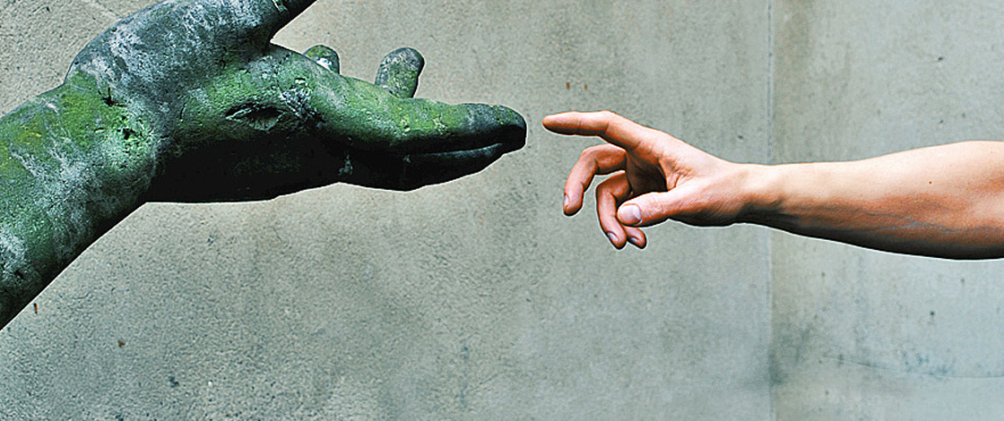 Menschliche Hand reicht Hand an einer Steinstatue